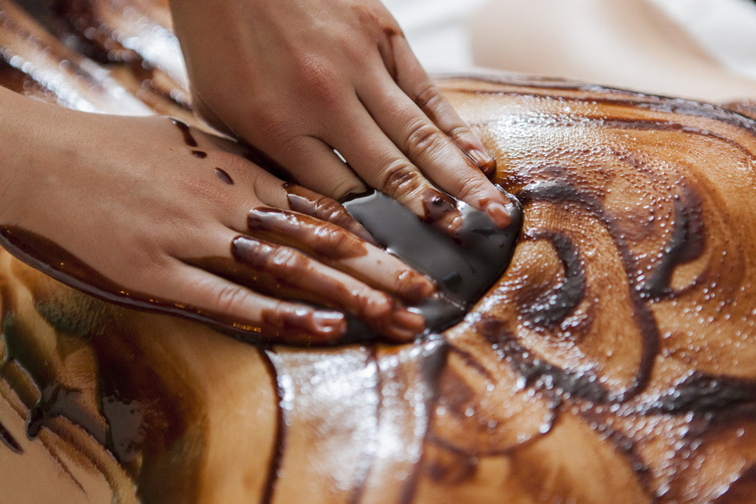 Czekoladowy masaż pleców z użyciem kamienia, dłonie masażysty rozprowadzają czekoladę po skórze.