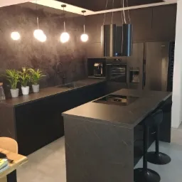 Nowoczesna kuchnia w odcieniach szarości i czerni z wyspą kuchenną, oświetleniem punktowym i dekoracyjną ścianą z fakturą.