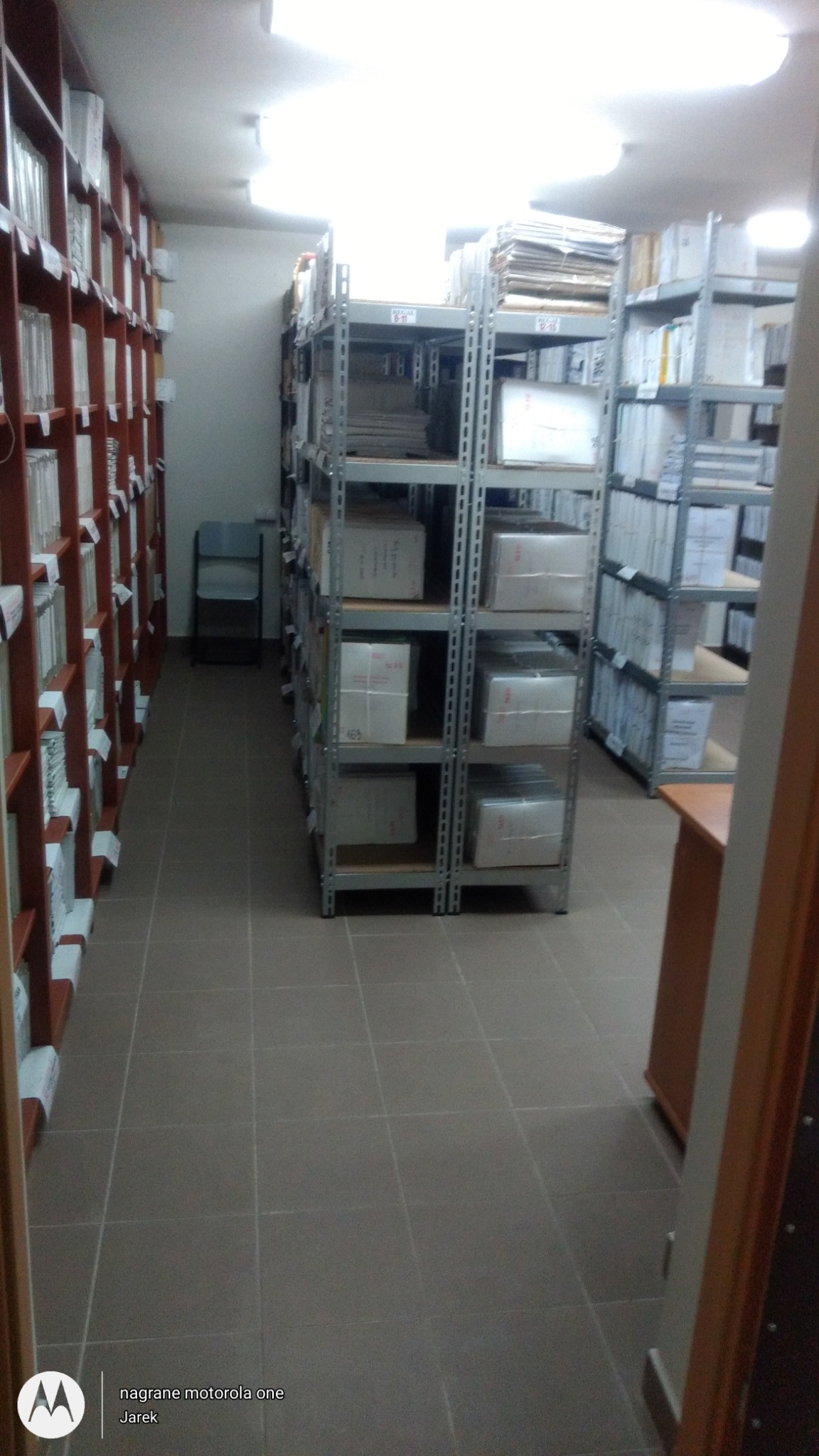 Magazyn dokumentów w Kielcach: Półki regałowe wypełnione segregatorami i zapakowanymi paczkami, widoczne także metalowe regały z dokumentami.