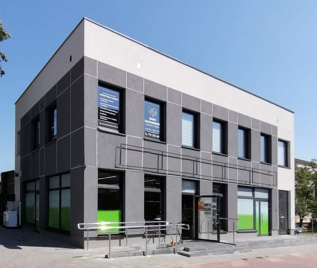 Nowoczesny budynek biurowy w odcieniach szarości z dużymi oknami, na których widoczne są plakaty informacyjne, w tym logo i dane kontaktowe firmy.