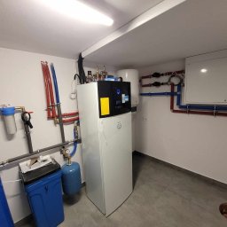 Soltimus Sp. z o.o. - Wnętrze kotłowni z zainstalowaną białą pompą ciepła Daikin, zbiornikiem buforowym, systemem filtrów wody i rozbudowaną instalacją hydrauliczną z rur miedzianych i plastikowych.