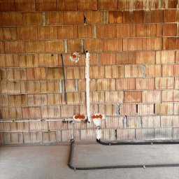 Mały Elektryk - Ściana z pustaków z instalacją elektryczną: rurki, kable w peszlach i pomarańczowe puszki pod gniazdka, zamocowane do ściany. Widok na surową instalację przed tynkowaniem.