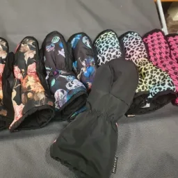 Różnokolorowe, wzorzyste rękawice dziecięce typu łapawice, z motywami kwiatowymi, kosmicznymi, panterki i pepitki, leżące na szarym tle.