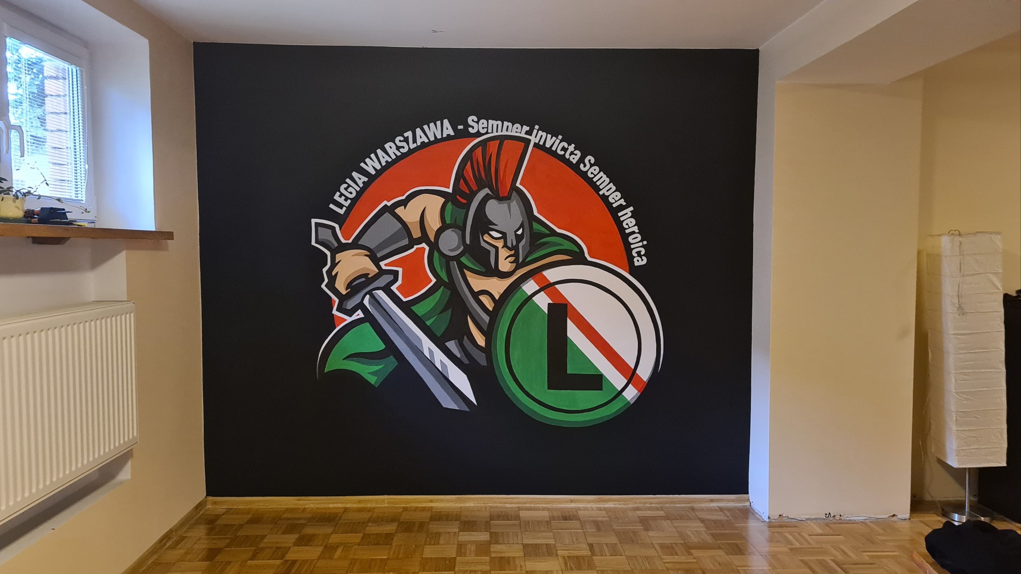 Malowidło ścienne przedstawiające stylizowanego rzymskiego legionistę z mieczem i tarczą z logiem Legii Warszawa na czarnym tle ściany w pokoju.