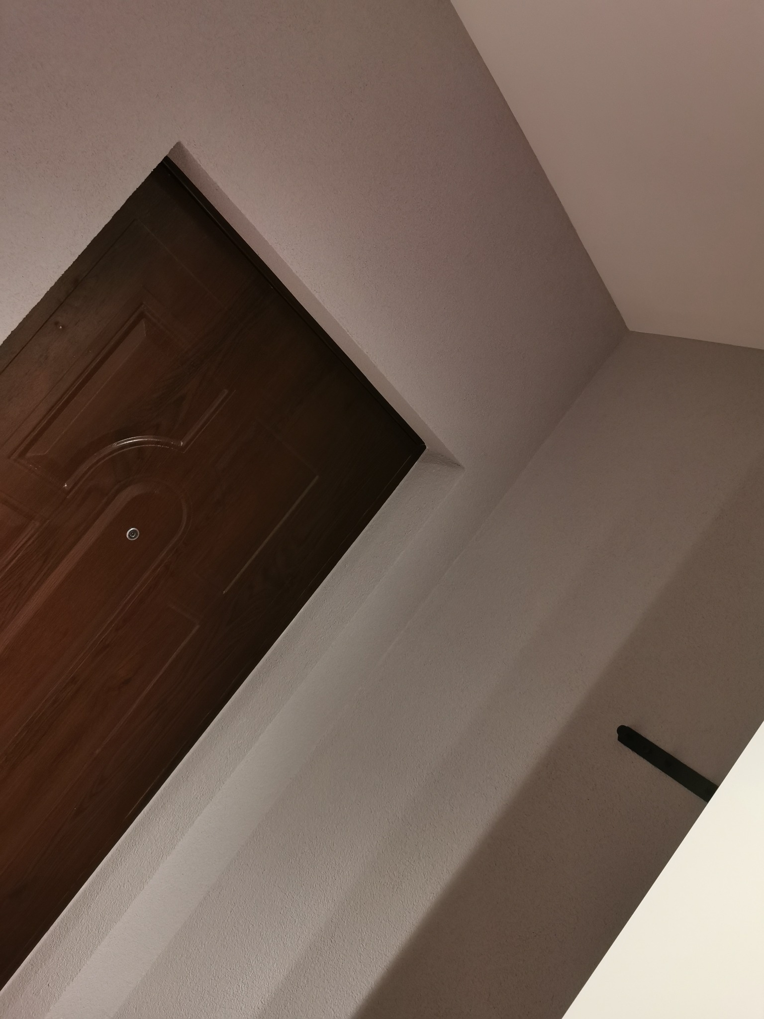 Ciemne, drewniane drzwi wejściowe z wizjerem, widziane z dołu, z fragmentem pomalowanego na biało sufitu i ściany.