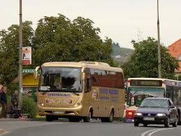Złoty autobus turystyczny z napisem 'Intertour 2010' na boku, zaparkowany na tle zieleni miejskiej i innych pojazdów, widziany z perspektywy ulicy.