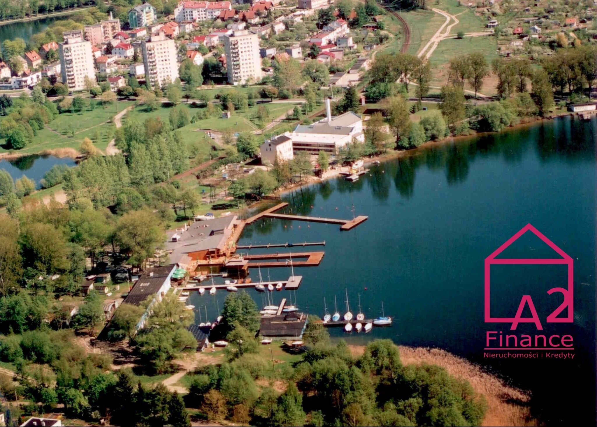 Panorama miasta z widokiem na jezioro, przystań jachtową i budynki mieszkalne, w tle logo firmy A2 Finance.