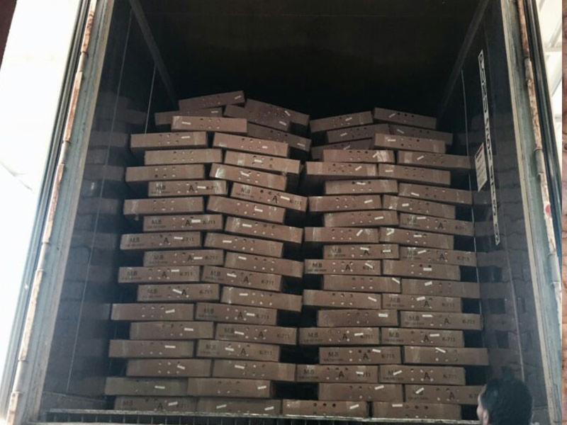 Pełny kontener załadowany paletami z brązowymi boksami, widoczne oznaczenia na każdym boksie, fragment sylwetki osoby z prawej strony.