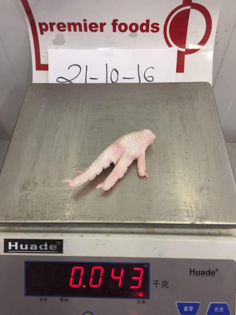 Pojedyncza, surowa kurza łapka ważąca 0.043 kg, umieszczona na wadze elektronicznej marki Huade, z widocznym napisem 'premier foods' i datą '21-10-16' w tle.