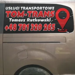 Boczny widok brązowego samochodu dostawczego z naklejką informacyjną 'Usługi Transportowe TOM-TRANS Tomasz Rutkowski +48 781 320 265' i czerwoną ikoną lokalizacji.