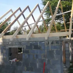 Budowa domu w Istebnej: surowa konstrukcja z bloczków i drewniana więźba dachowa w trakcie montażu, widoczne narzędzia i poziomica.