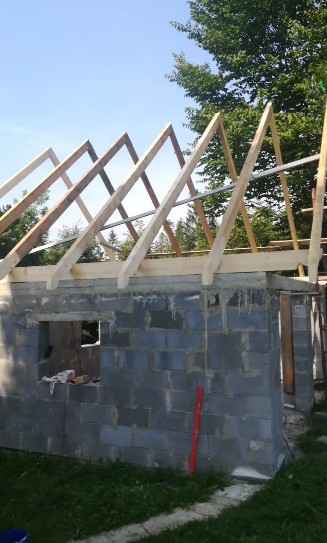 Budowa domu w Istebnej: surowa konstrukcja z bloczków i drewniana więźba dachowa w trakcie montażu, widoczne narzędzia i poziomica.