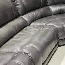 Fragment szarej, skórzanej sofy z dekoracyjnymi przeszyciami jasną nicią, widoczny z bliska.