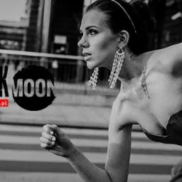 Czarno-białe ujęcie kobiety w sukni i z długimi kolczykami biegnącej przez przejście dla pieszych na tle miejskiej zabudowy z widocznym logo 'The Black Moon Film'.