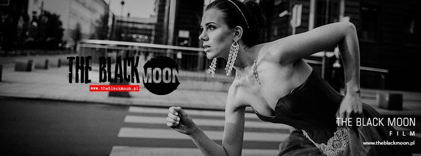 Czarno-białe ujęcie kobiety w sukni i z długimi kolczykami biegnącej przez przejście dla pieszych na tle miejskiej zabudowy z widocznym logo 'The Black Moon Film'.