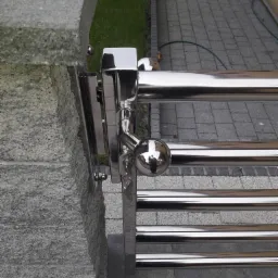 Fragment ogrodzenia ze stali nierdzewnej z kulistą gałką i kluczykiem przy bramie w Kiełpinie, widoczne mocowanie do kamiennego słupka.