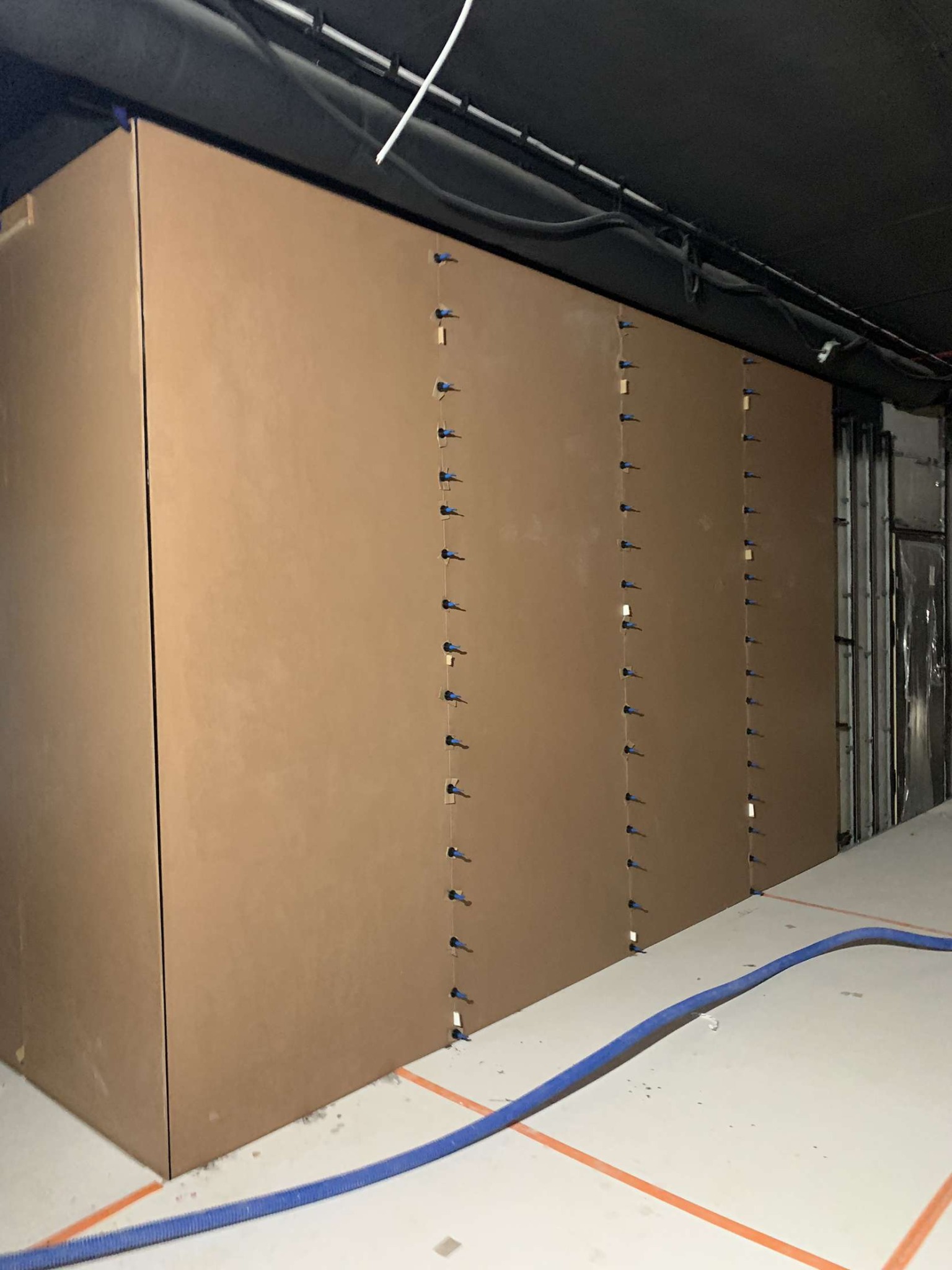 Przygotowanie ścian do malowania biura, zabezpieczone kartonem i przymocowane kołkami, widoczny wąż od odkurzacza na podłodze.