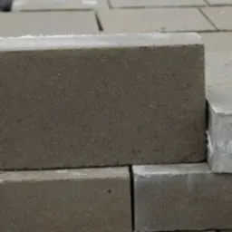 Ułożone w stosy szare betonowe bloczki z widocznymi śladami wilgoci i śniegu w tle.