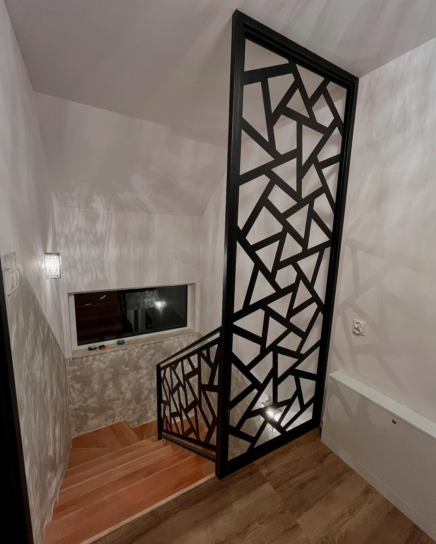 Nowoczesne schody z metalową balustradą o geometrycznym wzorze, czarna rama, drewniane stopnie, widok z góry, oświetlenie punktowe, jasne ściany.