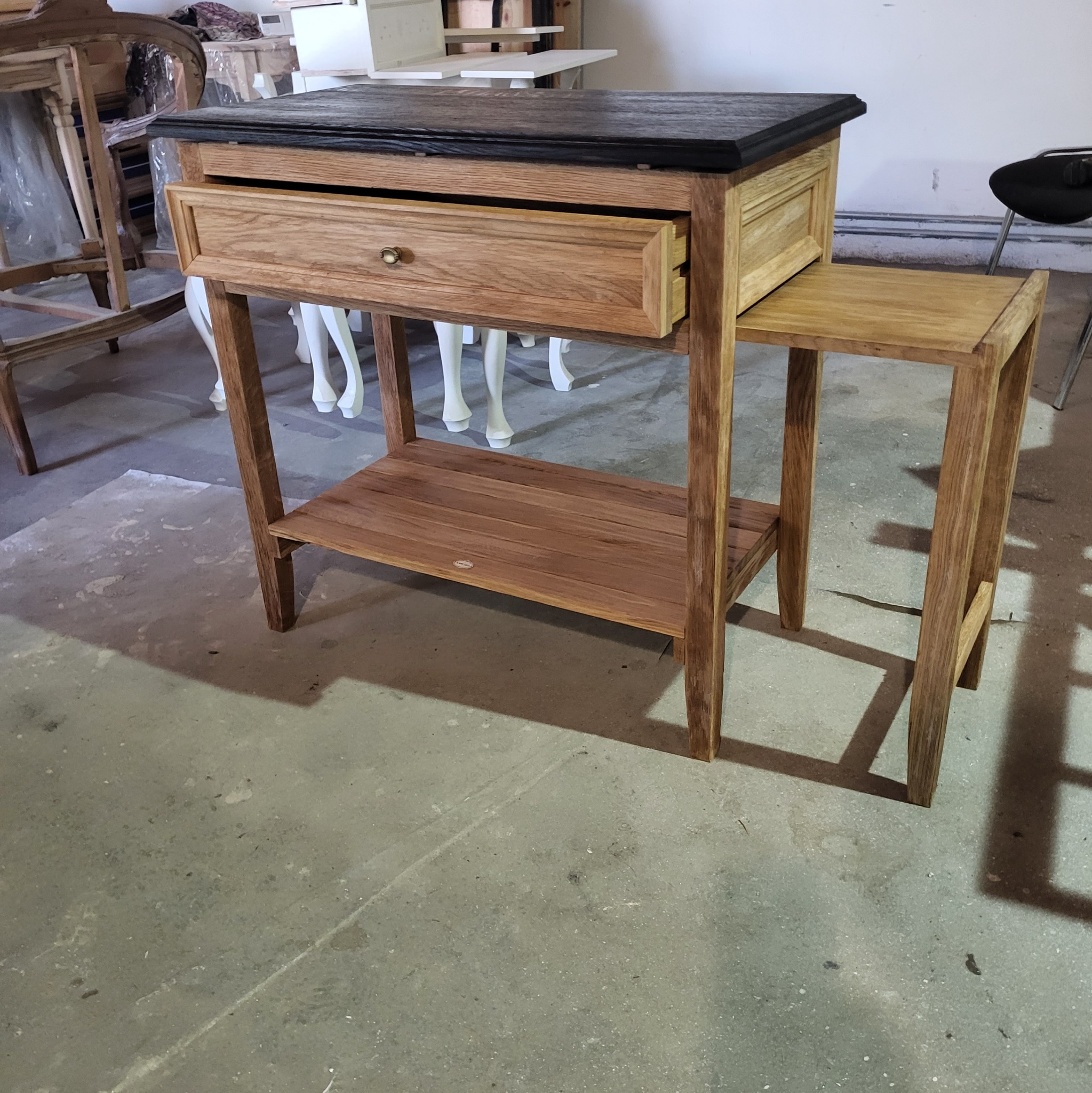 Dwu-poziomowy, rustykalny stolik z drewna dębowego z wysuwaną szufladą i czarnym blatem, widoczny w warsztacie.
