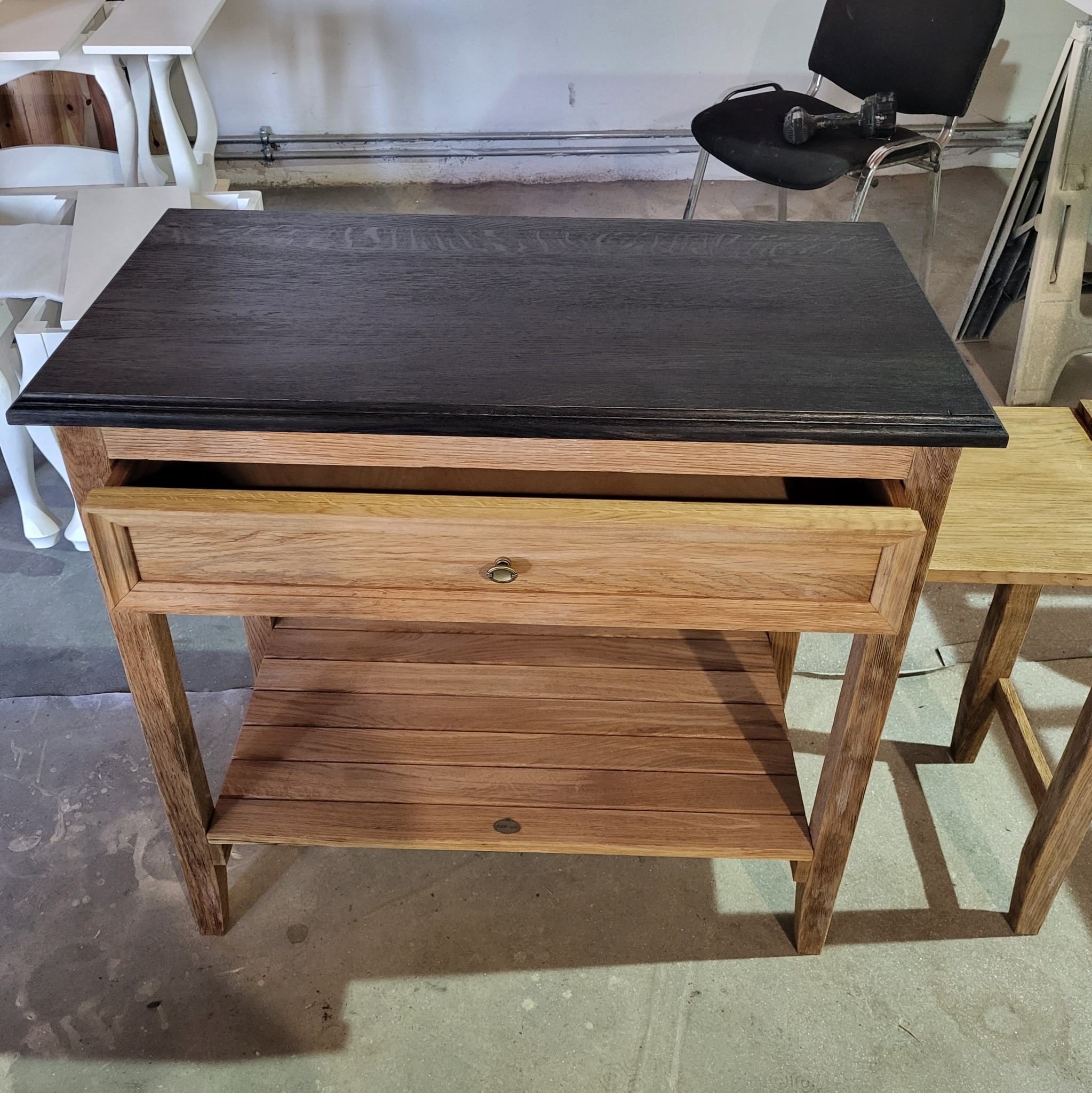 Drewniany stolik z szufladą i półką w Libertowie, blat w kolorze ciemnego dębu, korpus z jasnego drewna. Na blacie leży wiertarka akumulatorowa.