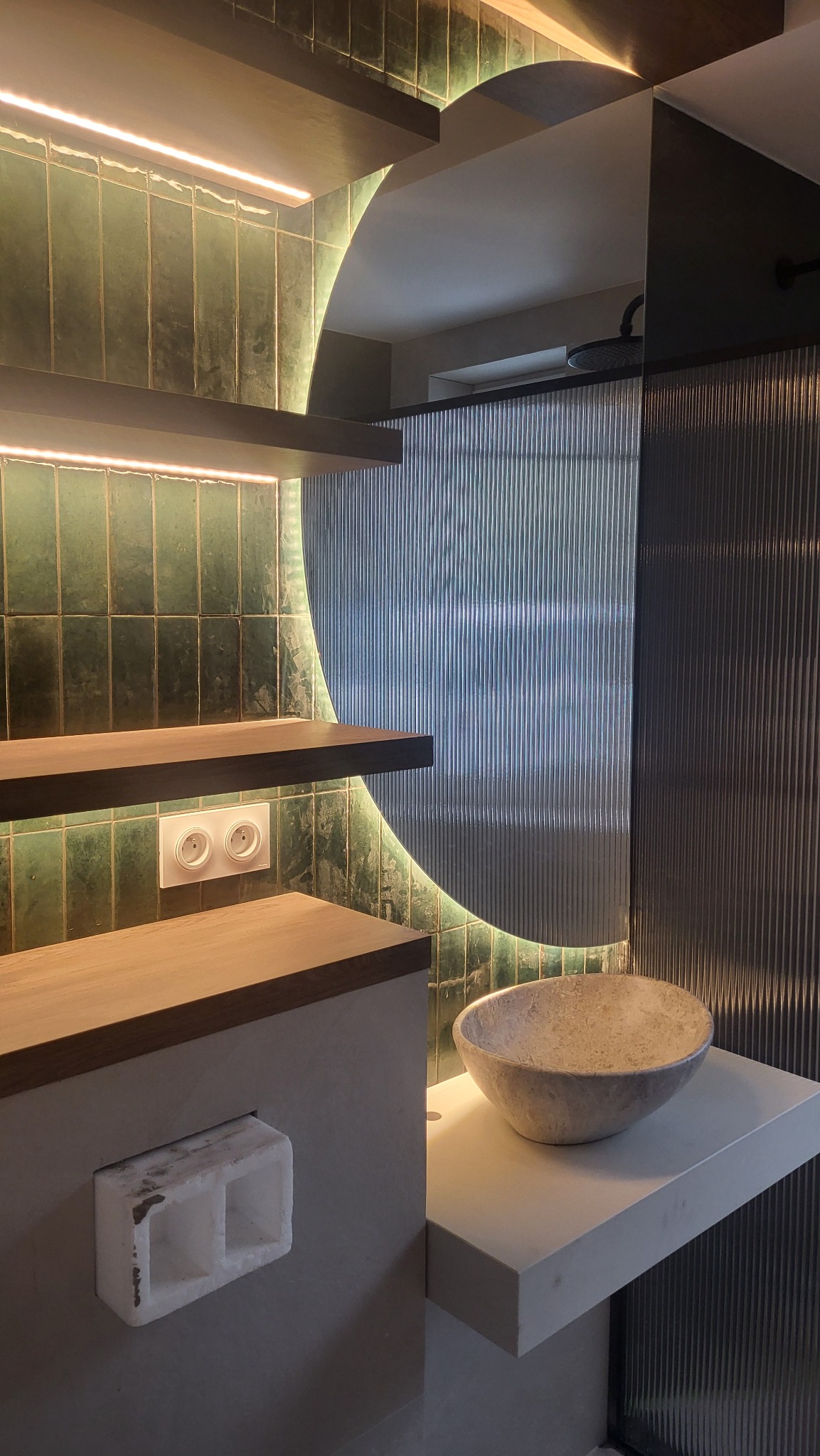 Nowoczesna łazienka z zielonymi płytkami, podświetlanymi półkami, umywalką w kształcie misy i szklaną ścianką prysznicową z ryflowanego szkła.