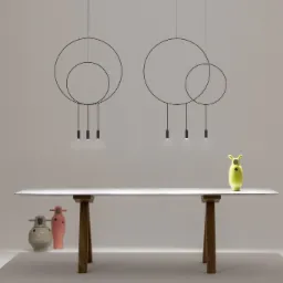 Dwa nowoczesne, okrągłe żyrandole z czarnymi obwodami i trzema punktami świetlnymi każdy, zawieszone nad białym stołem z drewnianymi nogami. Na stole stoi zielona, designerska figurka, a pod stołem...