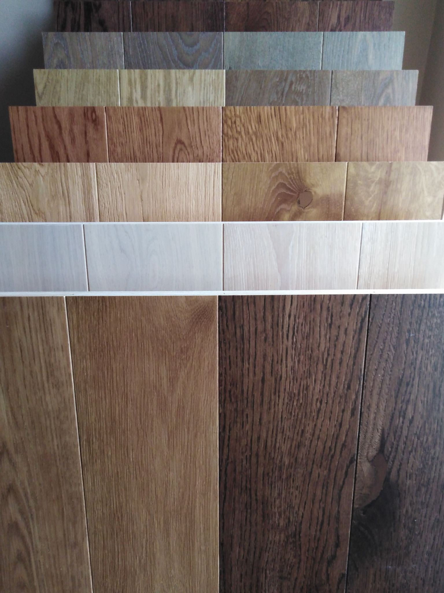 Ekspozycja próbek różnorodnych odcieni i wzorów paneli podłogowych, ułożonych warstwowo, ukazująca bogactwo faktur i kolorów drewna.