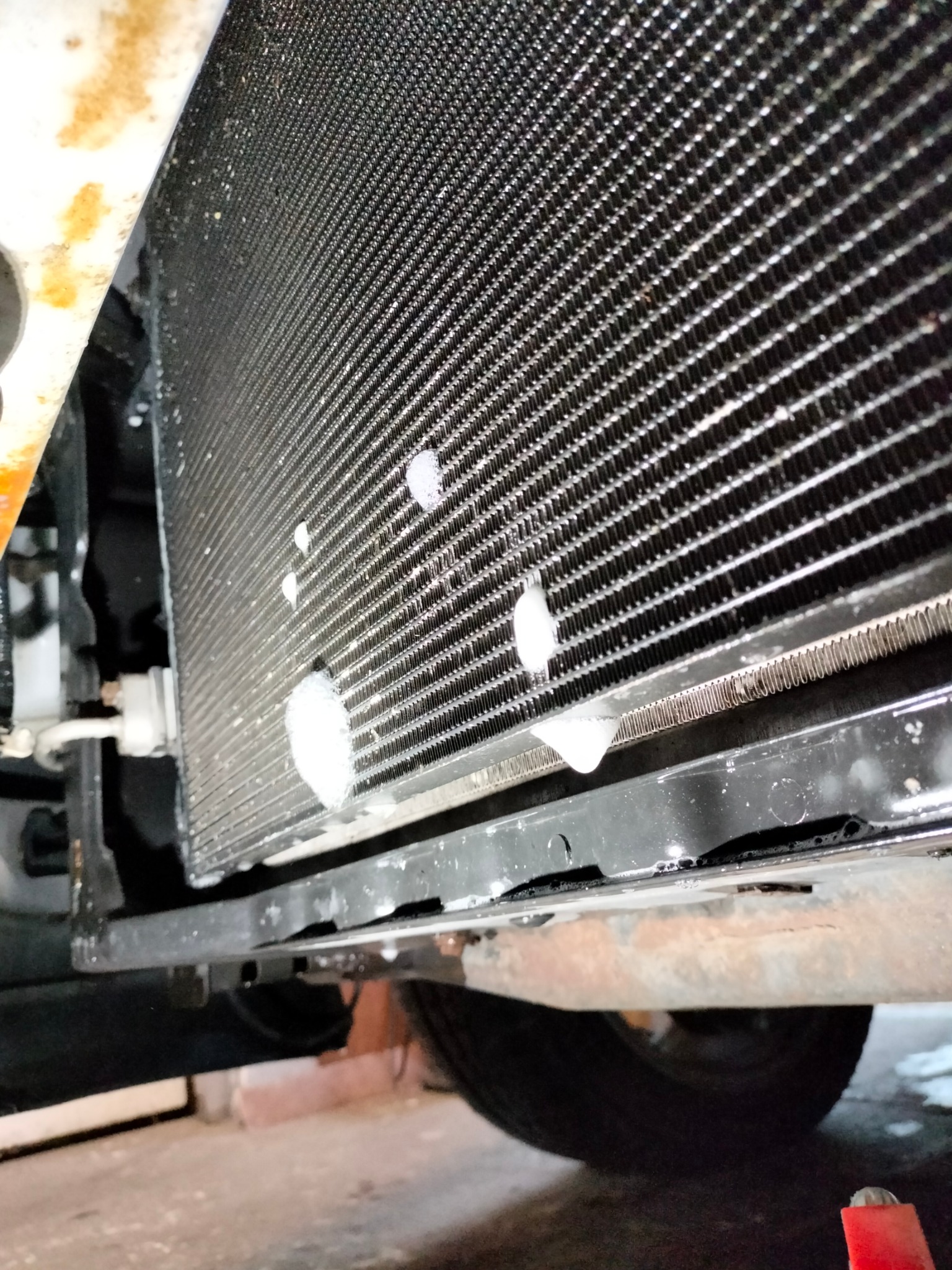 Wyciek czynnika chłodniczego z chłodnicy samochodowej, widoczne białe plamy na żeberkach chłodnicy, ujęcie od dołu.