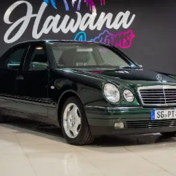 Zielony Mercedes-Benz W210 na tle ściany z logo 'Hawana Customs', widoczne detale chromowane i aluminiowe felgi.