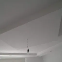 Nowoczesny sufit podwieszany z płyt kartonowo-gipsowych w odcieniach bieli, z widoczną żarówką na kablu, sugerujący etap prac wykończeniowych.