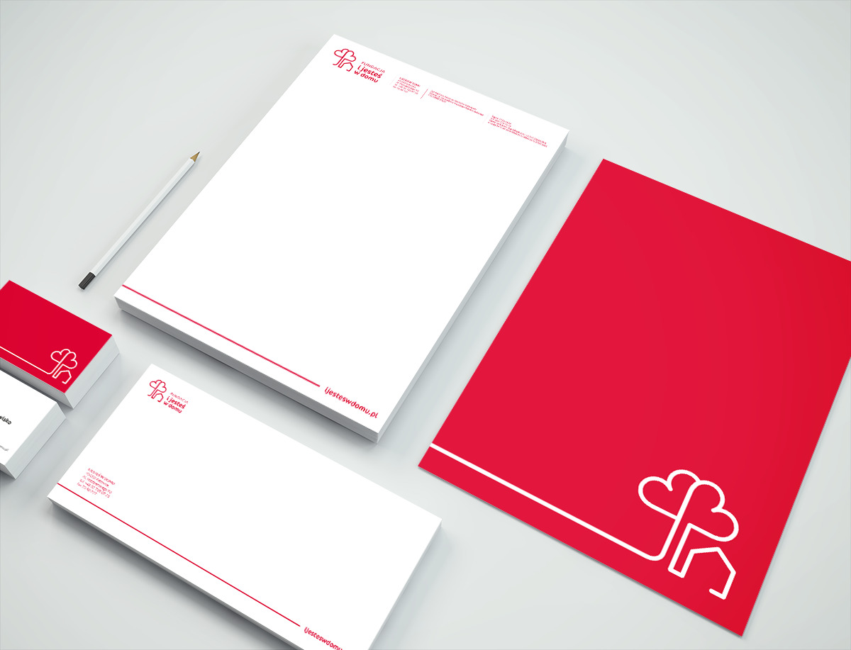 Zestaw materiałów firmowych w kolorze czerwono-białym, zawierający wizytówki, papier firmowy i kopertę, z logo w kształcie domu i serca, ułożony na jasnym tle z ołówkiem.