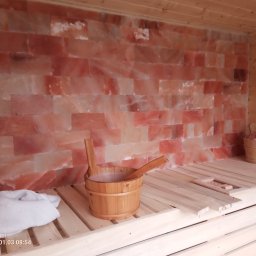 Nowi-Rem Paweł Nowicki - Wnętrze sauny z drewnianymi ławami, ścianą z bloków soli himalajskiej, drewnianym wiadrem z chochlą i miską z solą na ławie. Oświetlenie punktowe podkreśla fakturę soli.