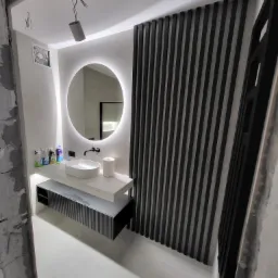 Nowoczesna łazienka w trakcie remontu: białe płytki, okrągłe lustro z podświetleniem LED, umywalka nablatowa, czarna armatura i dekoracyjna ścianka z pionowych, czarnych listew.