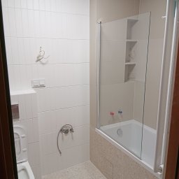 Nowi-Rem Paweł Nowicki - Jasna łazienka po remoncie: białe, pionowe płytki na ścianach, szklany parawan nawannowy, beżowa mozaika na obudowie wanny i jasna podłoga.