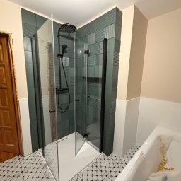 Nowi-Rem Paweł Nowicki - Nowoczesna kabina prysznicowa z czarnymi elementami, zielone płytki strukturalne, wzorzysta podłoga i drewniane drzwi w tle. Widok na fragment wanny.