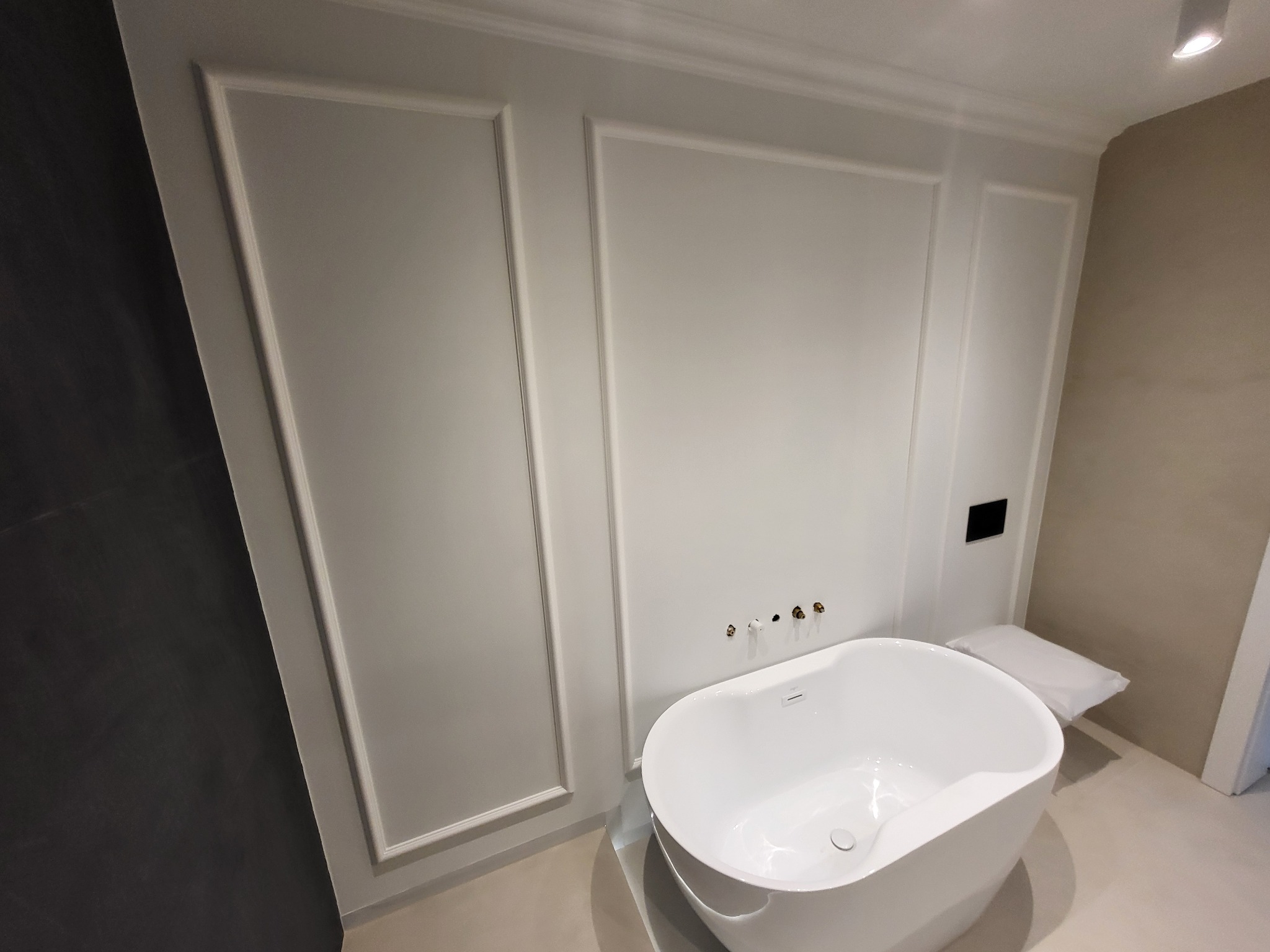 Nowoczesna, wolnostojąca wanna w minimalistycznej łazience z panelami ściennymi i złotymi elementami armatury.