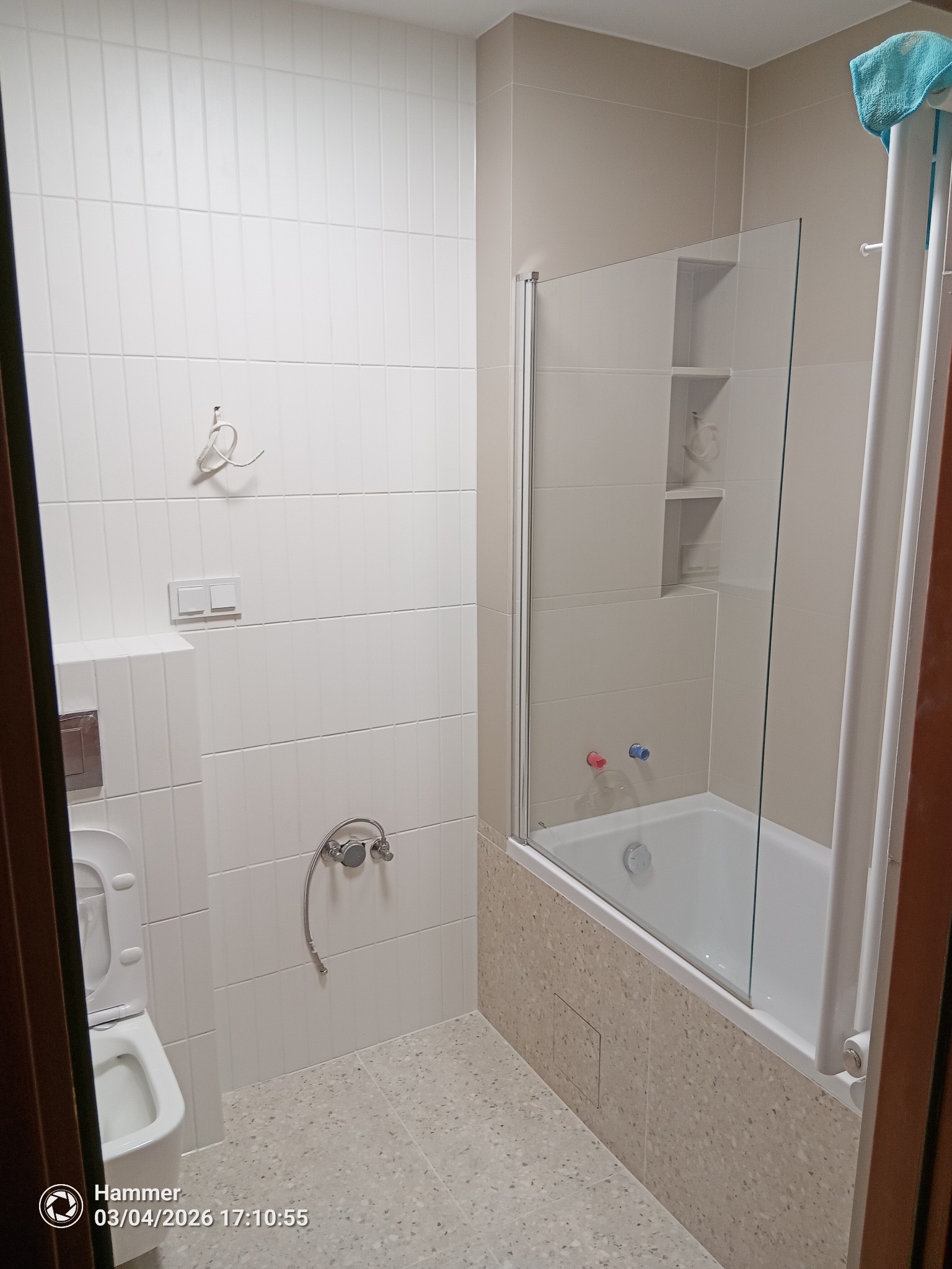 Jasna łazienka po remoncie: białe, pionowe płytki na ścianach, szklany parawan nawannowy, beżowa mozaika na obudowie wanny i jasna podłoga.