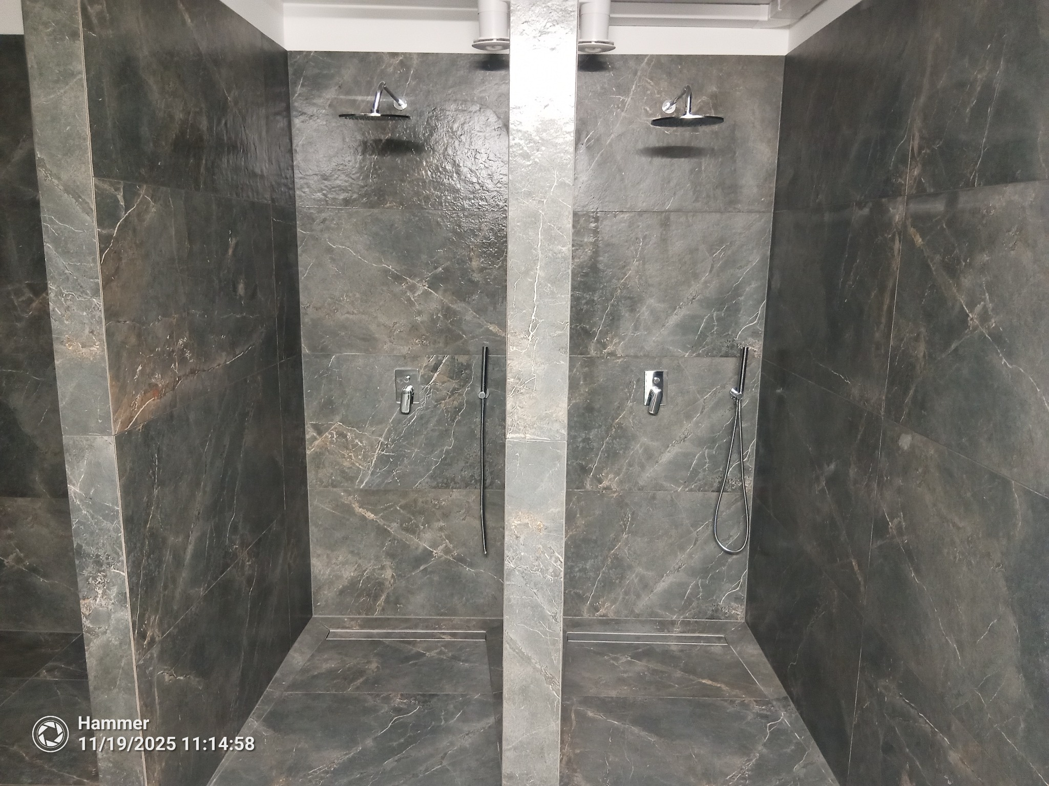 Nowoczesna kabina prysznicowa typu walk-in z szarymi płytkami imitującymi marmur, dwa zestawy natryskowe, minimalistyczny design, oświetlenie sufitowe.