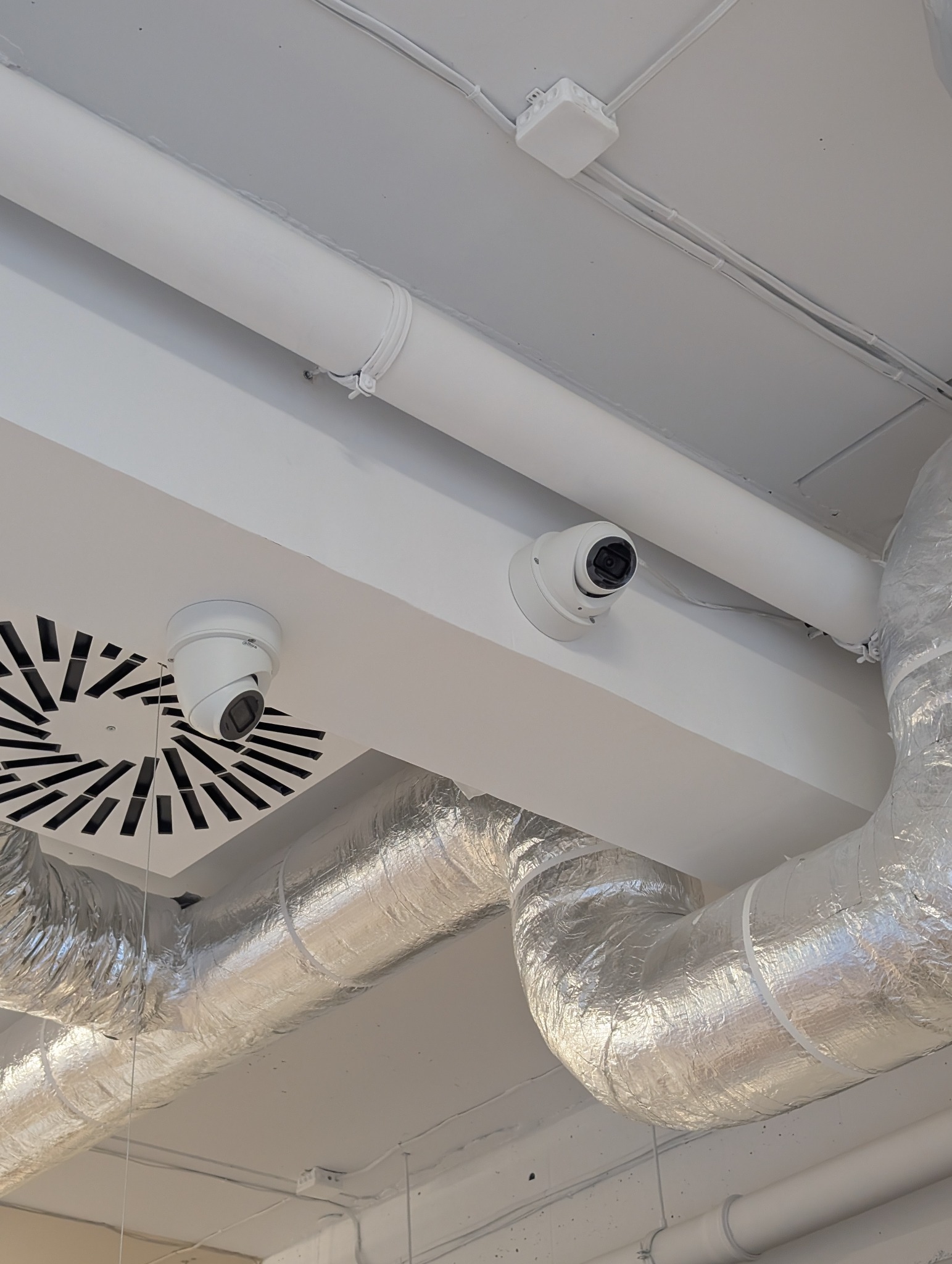 Dwie białe kamery kopułkowe zamontowane na suficie w pomieszczeniu z widocznymi rurami wentylacyjnymi i instalacją elektryczną.