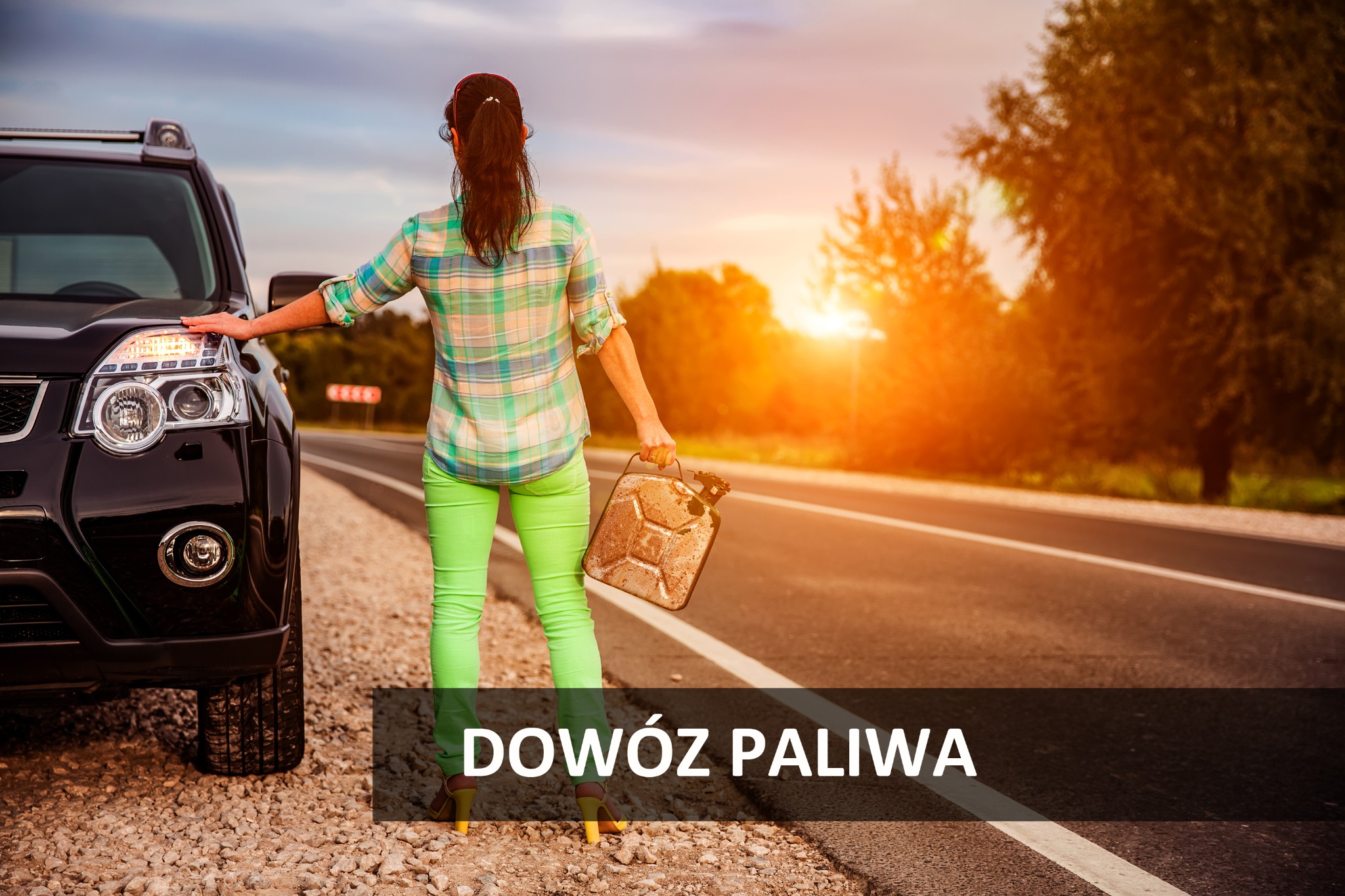 Kobieta w zielonych spodniach i kraciastej koszuli stoi tyłem przy czarnym samochodzie na poboczu drogi, trzymając w ręku kanister na paliwo, w tle zachodzące słońce.