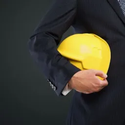 Mężczyzna w garniturze trzyma żółty kask budowlany na ciemnym tle.