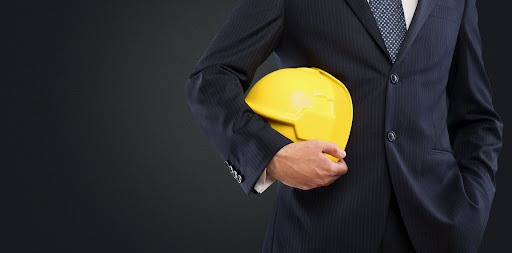 Mężczyzna w garniturze trzyma żółty kask budowlany na ciemnym tle.