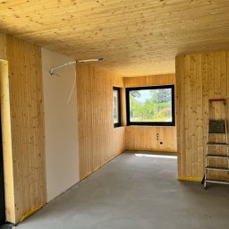 DOMY ENERGOOSZCZĘDNE, SZKIELETOWE TADEUSZ DORULA - Wnętrze w trakcie wykańczania: drewniana boazeria ścienna i sufitowa, fragment pomalowanej ściany, okno z widokiem na zieleń, drabina oparta o ścianę.