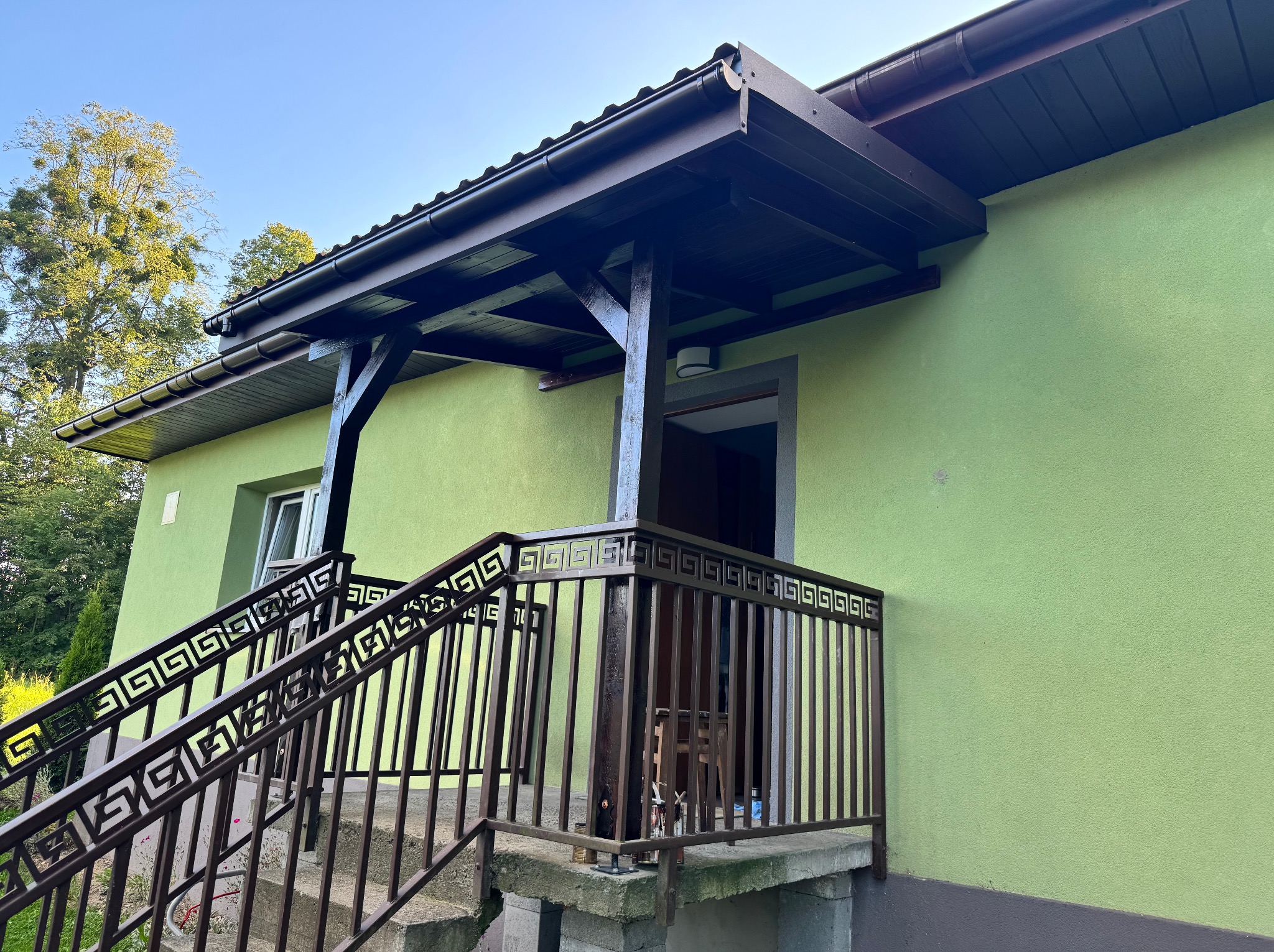 Zadaszone wejście do domu w Stryszowie z dekoracyjnymi balustradami schodów i balkonu, pomalowanego na zielono. Widok z dołu.