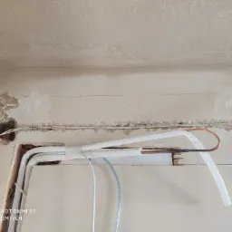 Instalacja rur miedzianych i przewodów w ścianie podczas montażu systemu chłodniczego, widoczne niedokończone wykończenie ściany i sufitu.