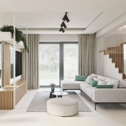 Lignum Design S.C. Monika Jakubowska Zbigniew Krupa - Jasne wnętrze salonu z drewnianymi schodami, szarą sofą narożną, stolikiem kawowym i regałem oddzielającym przestrzeń jadalną, oświetlone trzema reflektorami.