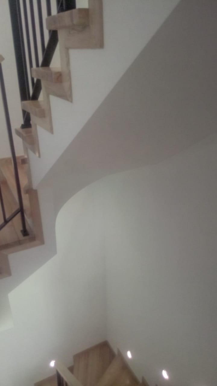 Klatka schodowa z drewnianymi stopniami i czarną metalową balustradą, widok z dołu, ściany wykończone gładzią.