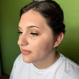 Profil kobiety z makijażem: złote cienie na powiekach, delikatny róż na policzkach i naturalne usta, włosy upięte do góry, zielone tło.