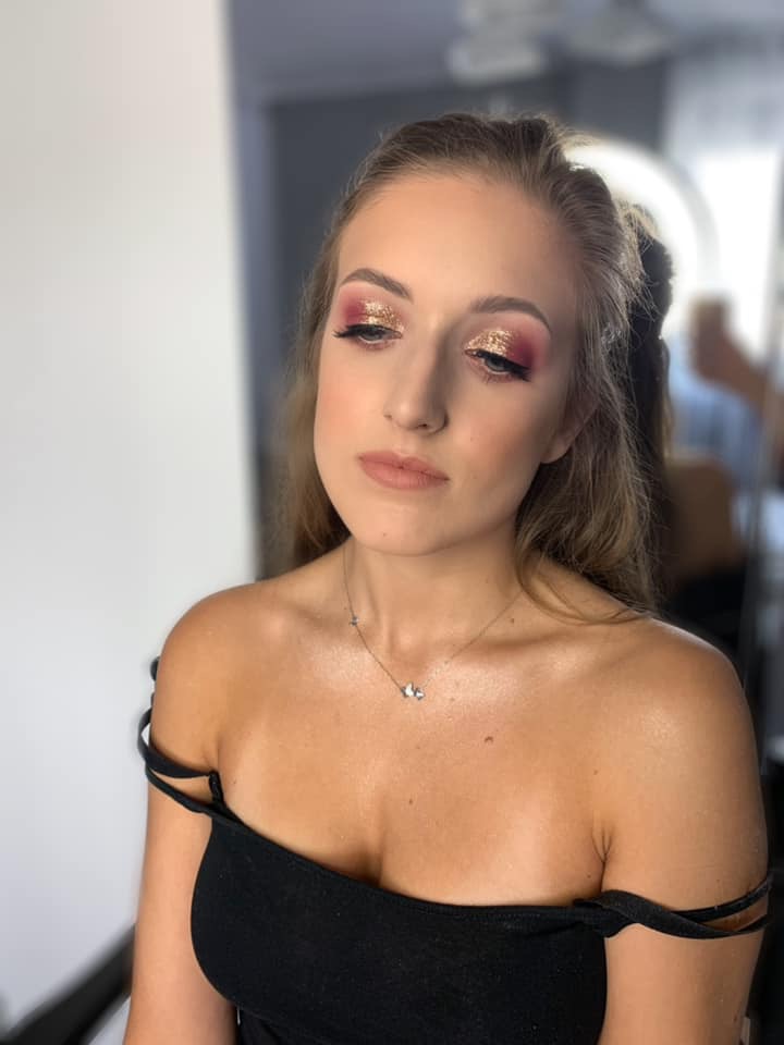 Portret kobiety z brokatowym cieniem do powiek w odcieniach różu i złota, delikatnym konturowaniem twarzy i subtelną szminką w odcieniu nude, z naszyjnikiem z zawieszkami w kształcie motyli.